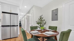 Una cocina moderna con un refrigerador de acero inoxidable, una mesa de comedor con sillas y una planta en maceta sobre la mesa.