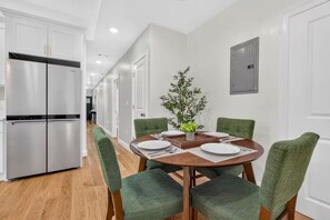 Une cuisine moderne avec un réfrigérateur en acier inoxydable, une table à manger avec des chaises et une plante en pot posée sur la table.