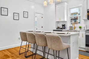 A modern kitchen with a central island, bar stools, white cabinetry, and pendant lighting. - 3BR/3Bth Somerville, 2 Parking Spots•Near Metro (Somerville)