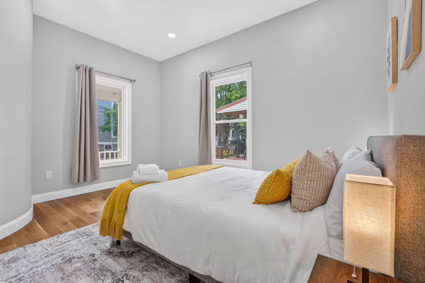 Un dormitorio con una cama grande, dos ventanas, vistas al exterior y piso de madera.
