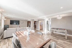A spacious living area with a dining table, sofa, and a foosball table. - Lake Surround House - Sleeps 11 • Boat Deck • BBQ (Georgina)