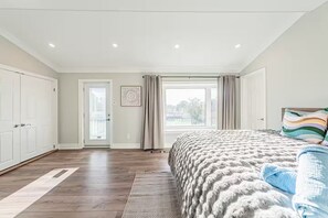 A bedroom with a large bed, a door leading to a balcony, and a view of the outdoors. - Lake Surround House - Sleeps 11 • Boat Deck • BBQ (Georgina)