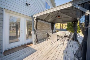 A covered patio with a table and chairs, a brick wall, and a sliding glass door. - Lake Surround House - Sleeps 11 • Boat Deck • BBQ (Georgina)