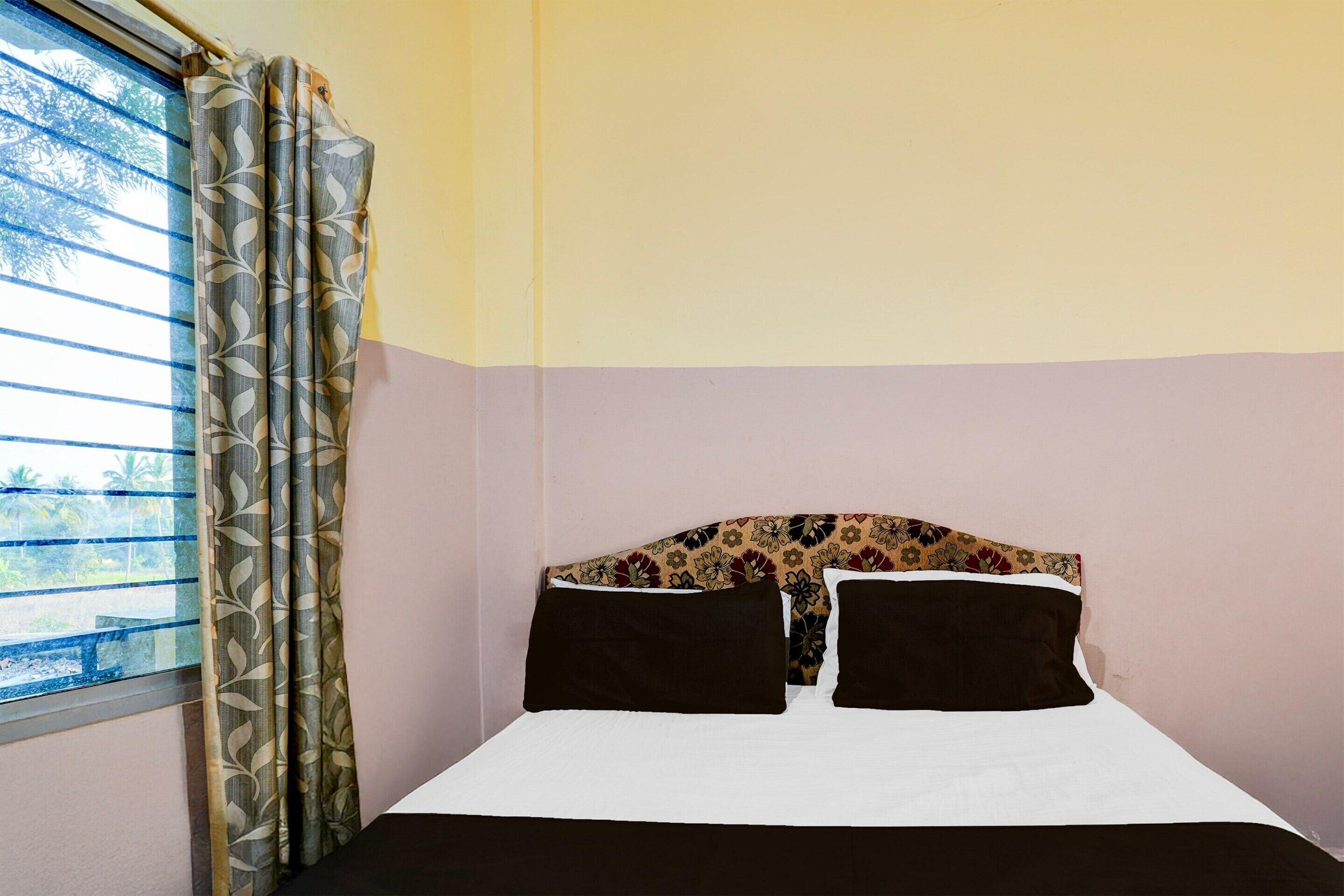 A bed with a patterned headboard, a window with curtains, and a view of palm trees.