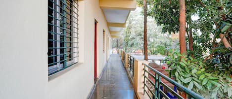 A corridor with a covered walkway, windows with metal bars, and a railing overlooking a garden.