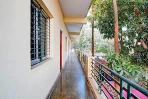 A corridor with a covered walkway, windows with metal bars, and a railing overlooking a garden.
