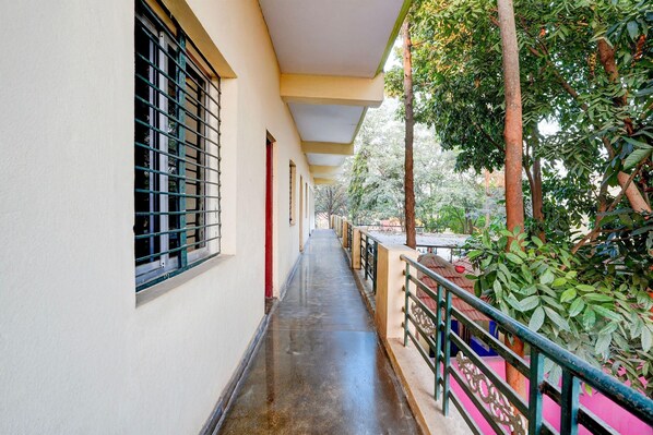 A corridor with a covered walkway, windows with metal bars, and a railing overlooking a garden. - Classic Mayuri Lodge (Bagepalli)