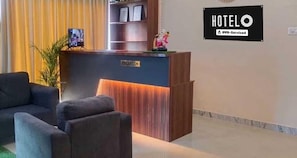 A hotel reception desk with a 'RECEPTION' sign, a framed picture, and a small statue on top. - Classic Mayuri Lodge (Bagepalli)