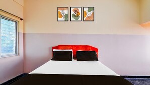 Un dormitori amb un llit, dos coixins, una finestra i tres quadres a la paret.