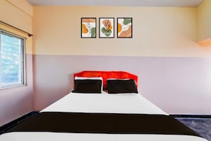 A bedroom with a bed, two pillows, a window, and three framed artworks on the wall.