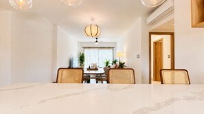 A dining area with a marble table, wicker chairs, a chandelier, and a view into the dining room. - Born | Modern 2BR with Pools | 6 Guests (Bavaro)