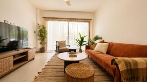 A living room with a television, sofa, coffee table, and potted plants. - Born | Modern 2BR with Pools | 6 Guests (Bavaro)