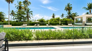 A swimming pool with lounge chairs and umbrellas, surrounded by palm trees and greenery. - Born | Modern 2BR with Pools | 6 Guests (Bavaro)