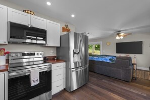 A modern kitchen with stainless steel appliances, a built-in oven, and a refrigerator. There is a dining area with a sofa and a flat-screen TV. - Pumpkintown Mountain View Cottage (Pickens)
