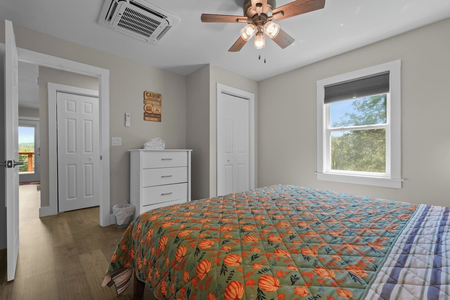 Ein Schlafzimmer mit Bett, Deckenventilator, Fenster und einer Tür, die auf einen Balkon führt.