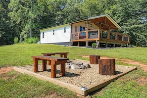 A two-story cabin with a deck, surrounded by a grassy yard and trees. - Pumpkintown Mountain View Cottage (Pickens)