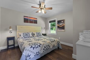 A bedroom with a bed, a nightstand, a bedside table, a ceiling fan, and artwork on the walls. - Pumpkintown Mountain View Cottage (Pickens)