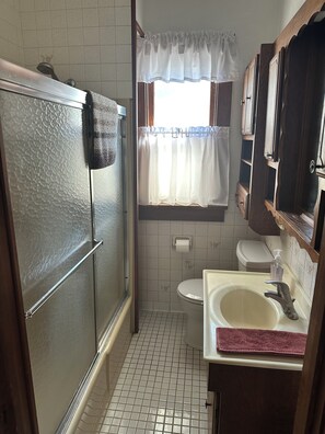 Et badeværelse med brusebad, toilet, håndvask og et vindue med gardin.