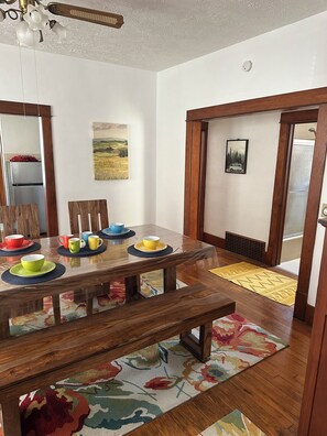 Un coin repas avec une table en bois dressée pour quatre personnes, un miroir et un ventilateur de plafond.