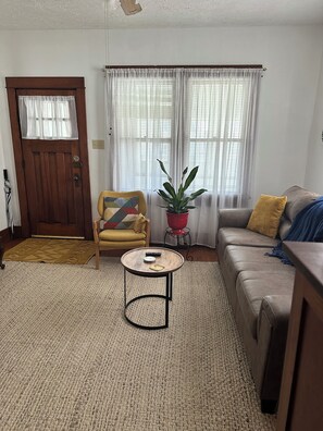 Una sala de estar con una puerta de madera, un sillón amarillo, un sofá marrón, una mesa de centro redonda y una planta en maceta.