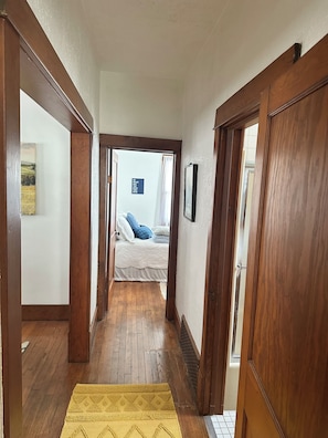 Un pasillo que conduce a un dormitorio con una cama, una puerta de madera y una alfombra amarilla.