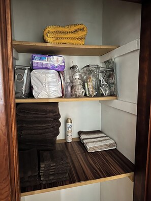 Un espace de rangement doté d’étagères où sont entreposées des serviettes, des articles de toilette et un objet enroulé.