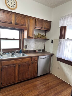 Una cocina con gabinetes de madera, un lavamanos de acero inoxidable y un lavavajillas.