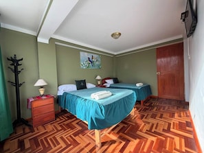 A hotel room with two beds, a wooden floor, a painting on the wall, and a door. - Rituales Inn San Borja  (Cusco)