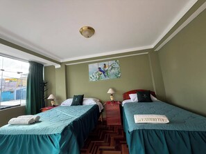 A hotel room with two beds, a window with curtains, a painting on the wall, and a ceiling light. - Rituales Inn San Borja  (Cusco)