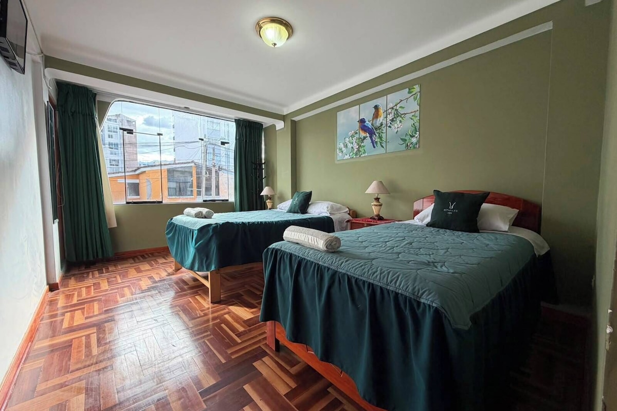A hotel room with two beds, a large window, a wooden parquet floor, and a painting on the wall.