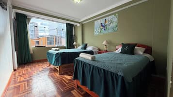 A hotel room with two beds, a large window, a wooden parquet floor, and a painting on the wall.
