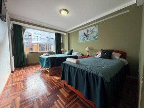 A hotel room with two beds, a large window, a wooden parquet floor, and a painting on the wall. - Rituales Inn San Borja (Cusco)