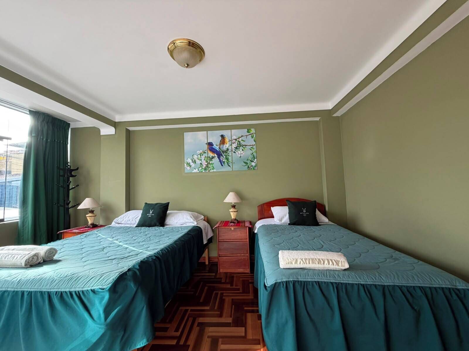 A hotel room with two beds, a painting on the wall, and a window with curtains.
