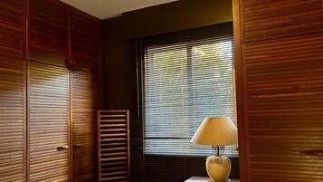 Una habitación con paneles de madera, una ventana con persianas, un sillón verde acolchado y una mesa con una lámpara.