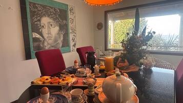 Una mesa de comedor dispuesta con platos, tazas y una tetera, con un cuadro y una ventana al fondo.