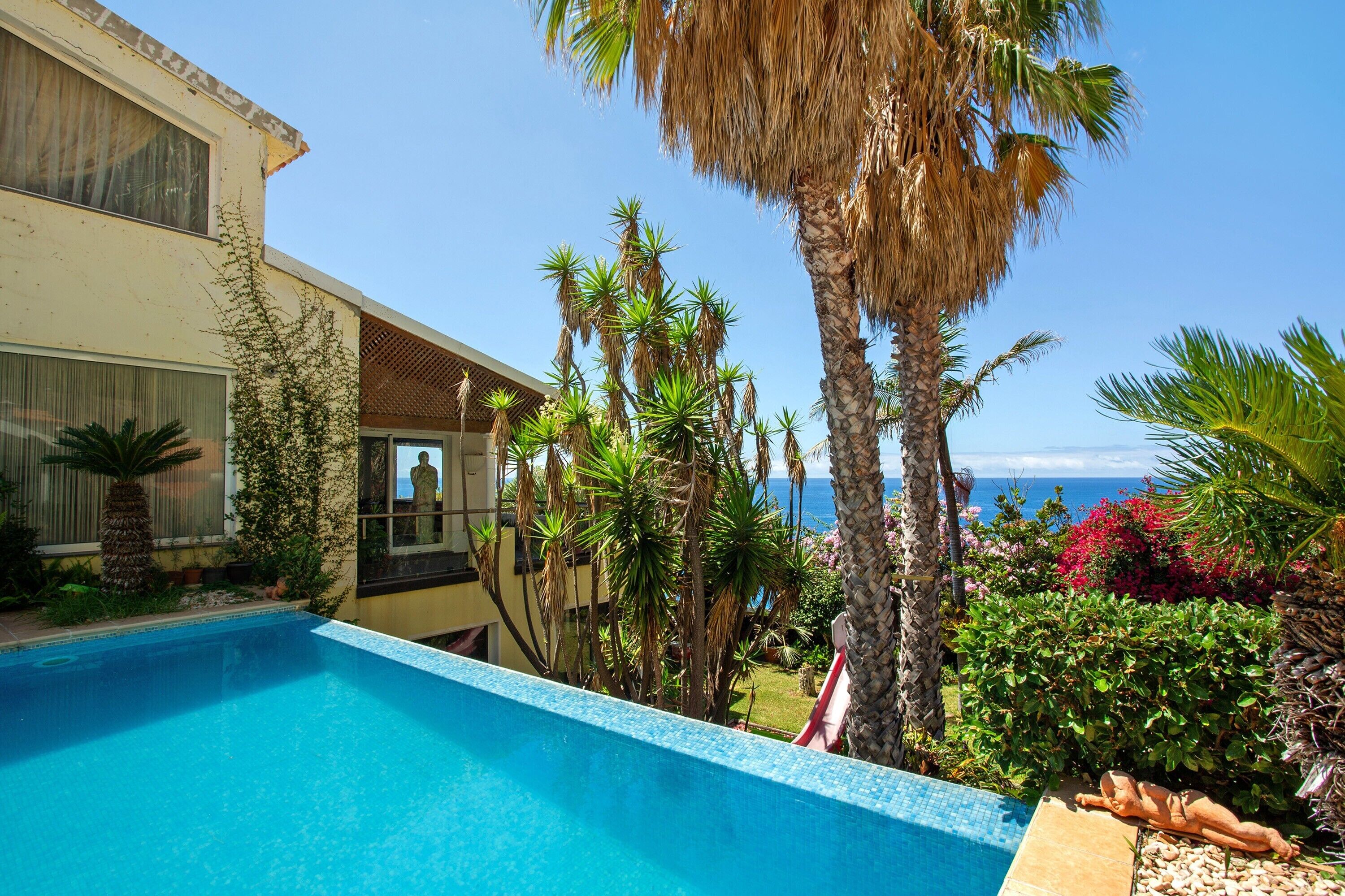 A poolside view with a clear sky, a building with a balcony, and a view of the ocean.