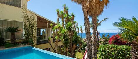 A poolside view with a clear sky, a building with a balcony, and a view of the ocean.
