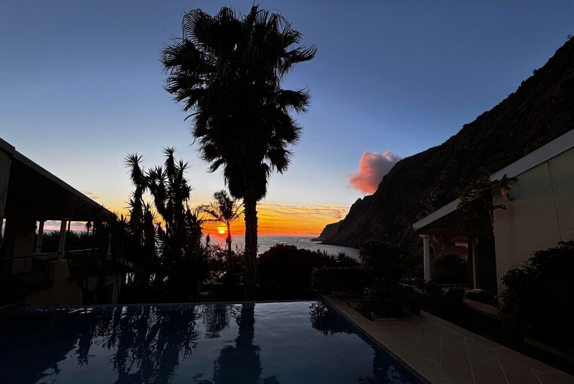 Ein Pool mit Sonnenuntergangsblick, Palmen und einem Bergpanorama.