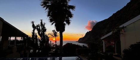 Ein Pool mit Sonnenuntergangsblick, Palmen und einem Bergpanorama.