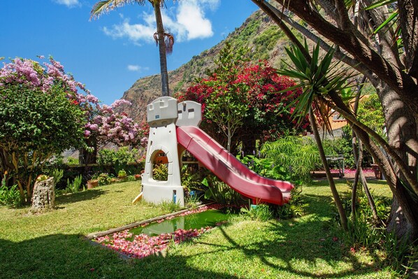 Un terrain de jeux avec un toboggan, entouré d’une végétation luxuriante et de plantes en fleurs.