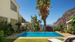A swimming pool with a view of the ocean, surrounded by palm trees and a hilly landscape. - Room 'Suite Vigia Jardim' with Sea View, Wi-Fi and Air Conditioning (Jardim do Mar)
