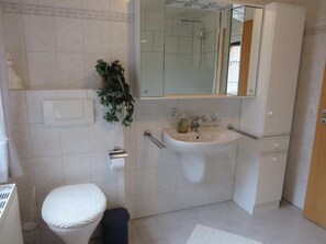 A bathroom with a white sink, a mirror, a toilet with a white seat, and a potted plant. - Vrbo Property (Aurich)
