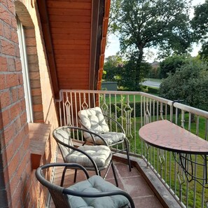 A balcony with two wicker chairs and a small table, overlooking a well-maintained garden and a road. - NEW! The Eisenhower Family Nest (Aurich)