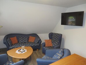 A room with a sofa, armchair, and a table with a glass and napkin. - Vrbo Property (Aurich)