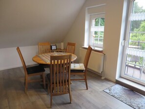 A dining area with a round table and four wooden chairs, a window with a view of greenery, and a radiator. - Vrbo Property (Aurich)