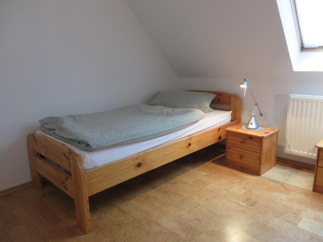 A single bed with a wooden frame, a bedside table with a lamp, and a radiator.