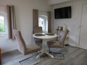 A room with a dining table and chairs, a television mounted on the wall, and a window with curtains. - NEW! Eisenhower's Cozy Nest (Aurich)