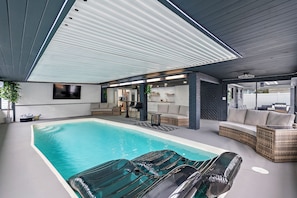 Un área de piscina interior con zona de descanso, asientos y un porche cubierto.