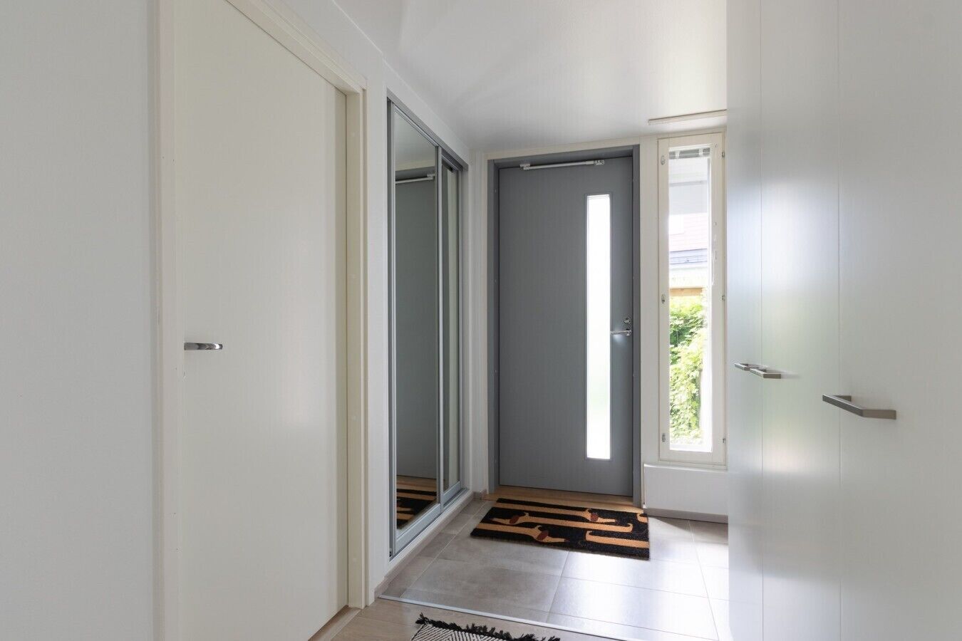 A hallway with a sliding glass door leading to a room, a door with a window, and a doormat on the floor.