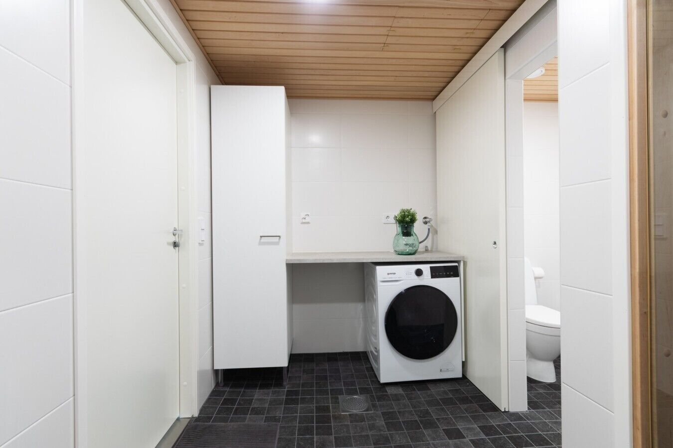 A compact laundry room with a washing machine, a small sink, and a toilet.